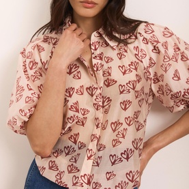 Model wearing Mint Velvet Heart Puff-Sleeve Shirt in pink with all-over heart print, classic collar and short puff sleeves, styled with blue jeans.