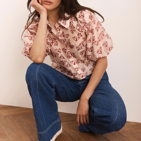 Model wearing Mint Velvet Heart Puff-Sleeve Shirt in pink with red heart print, classic collar, styled with blue wide-leg jeans.