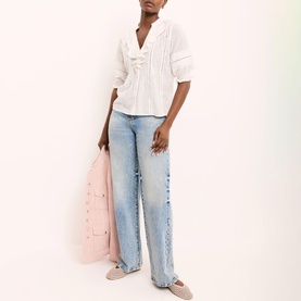 Model wearing Mint Velvet White Ruffle Trim Blouse with light wash wide-leg jeans, pink jacket and nude flat shoes