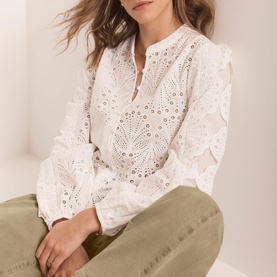 Model wearing Mint Velvet Shell Broderie Blouse in white with scallop trim and long sleeves, styled with olive green trousers.