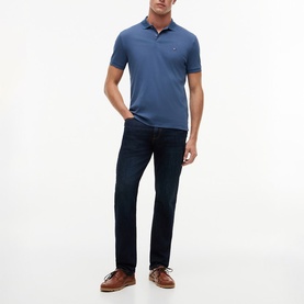 Model wearing a blue slim-fit polo shirt with small chest logo, styled with dark navy jeans and brown leather shoes.