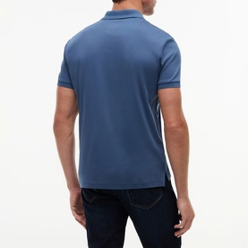 Model wearing blue polo shirt, back view, with contrast tipped collar and cuffs, styled with dark navy jeans.