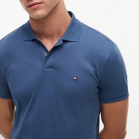 Model wearing a Tommy Hilfiger blue slim-fit polo shirt with embroidered flag logo and button placket neckline.