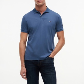 Model wearing blue short-sleeve polo shirt with signature flag logo, styled with dark navy jeans.