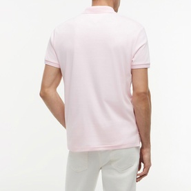 Model wearing Tommy Hilfiger Pink Lily polo shirt, rear view, with contrast tipping on collar and cuffs, paired with white trousers.