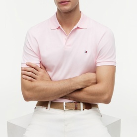 Model wearing Tommy Hilfiger polo shirt in Pink Lily with short sleeves and logo embroidery, styled with a beige woven belt.