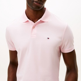 Model wearing Tommy Hilfiger polo shirt in Pink Lily, slim fit piqu&eacute; fabric with three-button placket and signature flag logo embroidery.