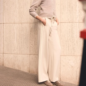 Model wearing Mint Velvet Cream Side Stripe Mid-Rise Wide Leg Trousers with a grey knit top and beige suede shoes.