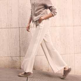 Model wearing Mint Velvet Cream Side Stripe Mid-Rise Wide Leg Trousers, styled with a grey knit top and taupe trainers.