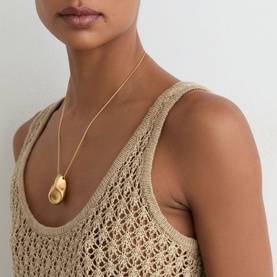 Model with gold-tone sculptural pendant necklace, styled with a beige open-knit crochet vest top