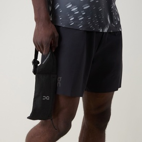 Model with On Running black accessory pouch held in hand, styled with black shorts and grey printed performance tee