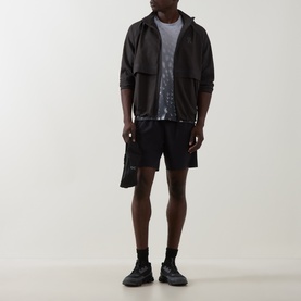Model wearing On Running Casual Jacket in Espresso, styled with black shorts, graphic tee and black trainers.
