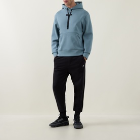 Model wearing On Running Hoodie in Agave blue with black joggers and black trainers.
