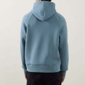 Model wearing On Running hoodie in Agave blue, back view, with dark trousers. Small logo detail at hem.