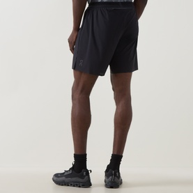 Model wearing On Running black performance shorts, styled with black socks and dark trainers, rear view showing relaxed fit