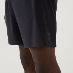 Model wearing On Running black performance shorts, lightweight with subtle logo detail, close-up mid-section view.