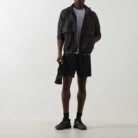Model wearing On Running black performance shorts with grey tee and dark zip-up jacket, styled with black trainers.