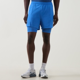 Model wearing On Running Jay Heather Performance Shorts in blue, featuring layered inner brief design, styled with white trainers.