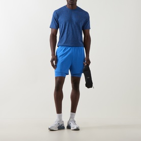 Model wearing On Running Jay Heather Shorts with matching blue tee and grey trainers, holding a black item at side.