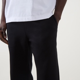 Model wearing On Running black sweatpants in cotton-polyester blend, wide-leg fit with side pocket, styled with white T-shirt.