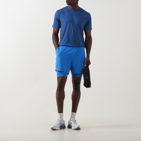 Model wearing On Running Jay Heather T-Shirt with matching blue shorts and white trainers, holding a jacket.