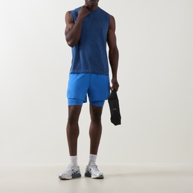 Model wearing On Running Jay Heather sleeveless T-shirt, styled with blue shorts, white socks and grey trainers, holding a black bag.