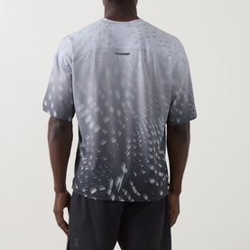 Model wearing On Running Performance T-Shirt in Espresso, rear view, with grey abstract gradient pattern and dark shorts.