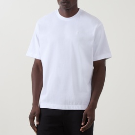 Model wearing On Running white cotton T-shirt with small chest logo, short sleeves, and crew neckline, styled with black trousers.