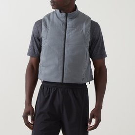Model wearing On Running silver performance gilet with zip front and high collar, styled with grey tee and black shorts