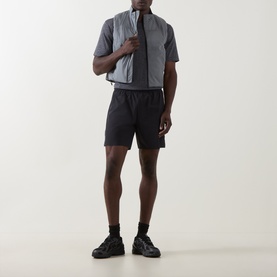 Model wearing On Running Silver performance gilet, styled with black shorts and black trainers.