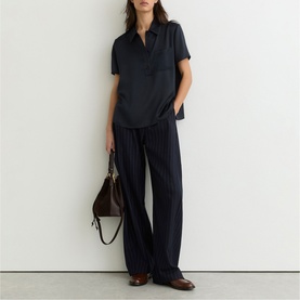 Model wearing Reiss blue short-sleeve collared shirt and wide-leg trousers, styled with brown leather bag and loafers