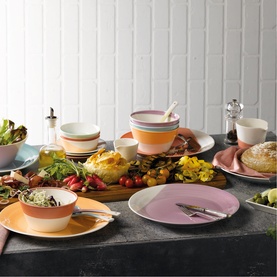 Royal Doulton multi-coloured dinnerware set styled on a table with food, featuring plates, bowls in pink, orange, blue and striped designs