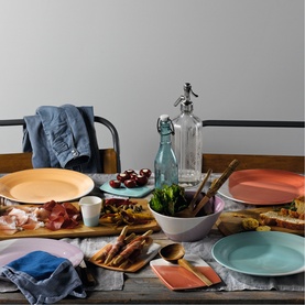 Royal Doulton multicoloured dinnerware set styled on a rustic wooden table with food, glassware, and linen napkins.