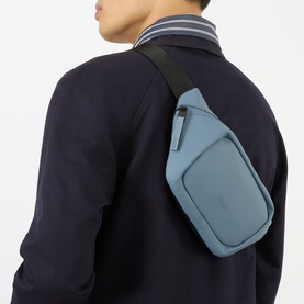Model carrying Rains Logo Waterproof Belt Bag in Blue Dusk, worn as crossbody with black adjustable webbing strap, styled with navy jacket.