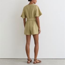 Model wearing Reiss green short-sleeve belted playsuit with flutter sleeves, styled with tan flat sandals, rear view