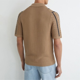 Model wearing Reiss light camel knit polo shirt, back view, showing open-knit panels and contrast stripe sleeve detail, styled with light blue jeans.