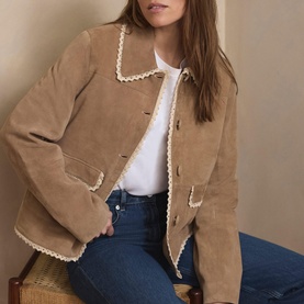 Model wearing camel suede jacket with cream lace trim detailing, styled with white top and blue jeans