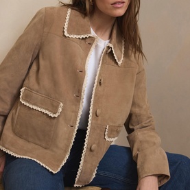 Model wearing tan suede jacket with cream scalloped trim, styled with white top and blue jeans