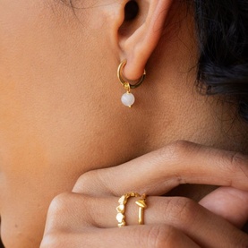 Model with Juvi gold hoop earrings featuring white pearl drop charm, styled with gold stacking rings