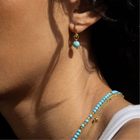 Model with Juvi gold drop earring featuring turquoise blue bead, styled with matching turquoise beaded necklace and gold chain necklace.