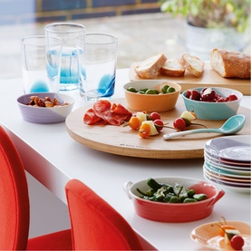Royal Doulton multi-coloured stoneware bowls and plates styled on a dining table with food, glassware, and a wooden serving board.