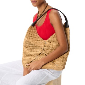 Model carrying Whistles beige crochet tote bag with black leather handles, styled with red top and white trousers