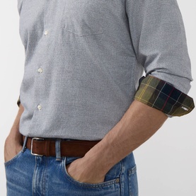 Model wearing Barbour navy cotton casual shirt with tartan cuff lining, rolled sleeves, styled with blue jeans and tan leather belt