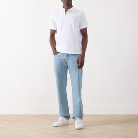 Model wearing Barbour white cotton polo shirt, styled with light wash straight-leg jeans and white trainers
