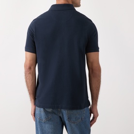 Model wearing Barbour navy cotton polo shirt, rear view, styled with light blue jeans