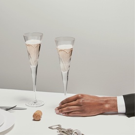 Waterford clear crystal champagne flutes filled with sparkling wine, styled on a white surface with a cork and a hand in frame