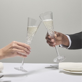 Waterford clear crystal champagne flutes with textured stems being clinked in a toast above a white table setting