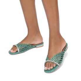 Model wearing green crystal-embellished flat slide sandals with woven cross-strap design and clear rhinestone trim on flat sole.