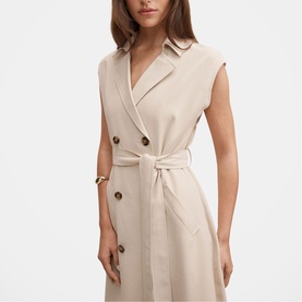 Model wearing a sleeveless beige double-breasted belted dress with notch lapel and gold-tone buttons