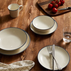 Gordon Ramsay dinnerware set in cream with blue rim, including dinner plate, bowl, side plate and mug, styled on wooden table